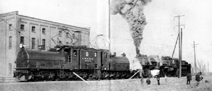 A 265-ton gearless passenger electric locomotive is seen pushing against a 278-ton freight steam locomotive.