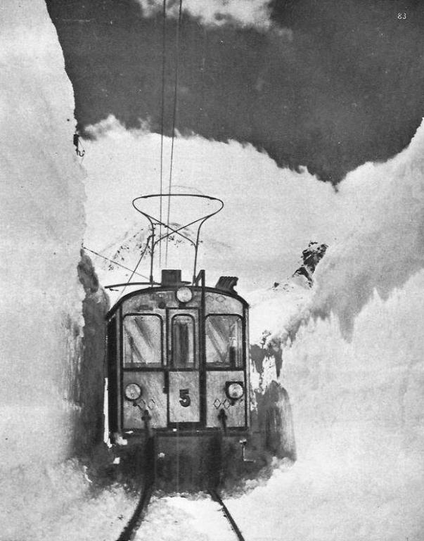 This electric train of the Swiss Federal Railways is able to travel on its Alpine journey only after a way has been cleared for it through the heavy drifts